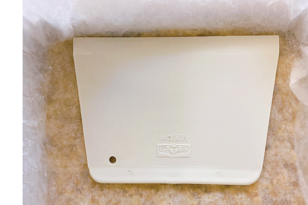 7.再蓋上一層烘焙紙，用刮刀往下壓，讓棉花糖玉米片密實結合